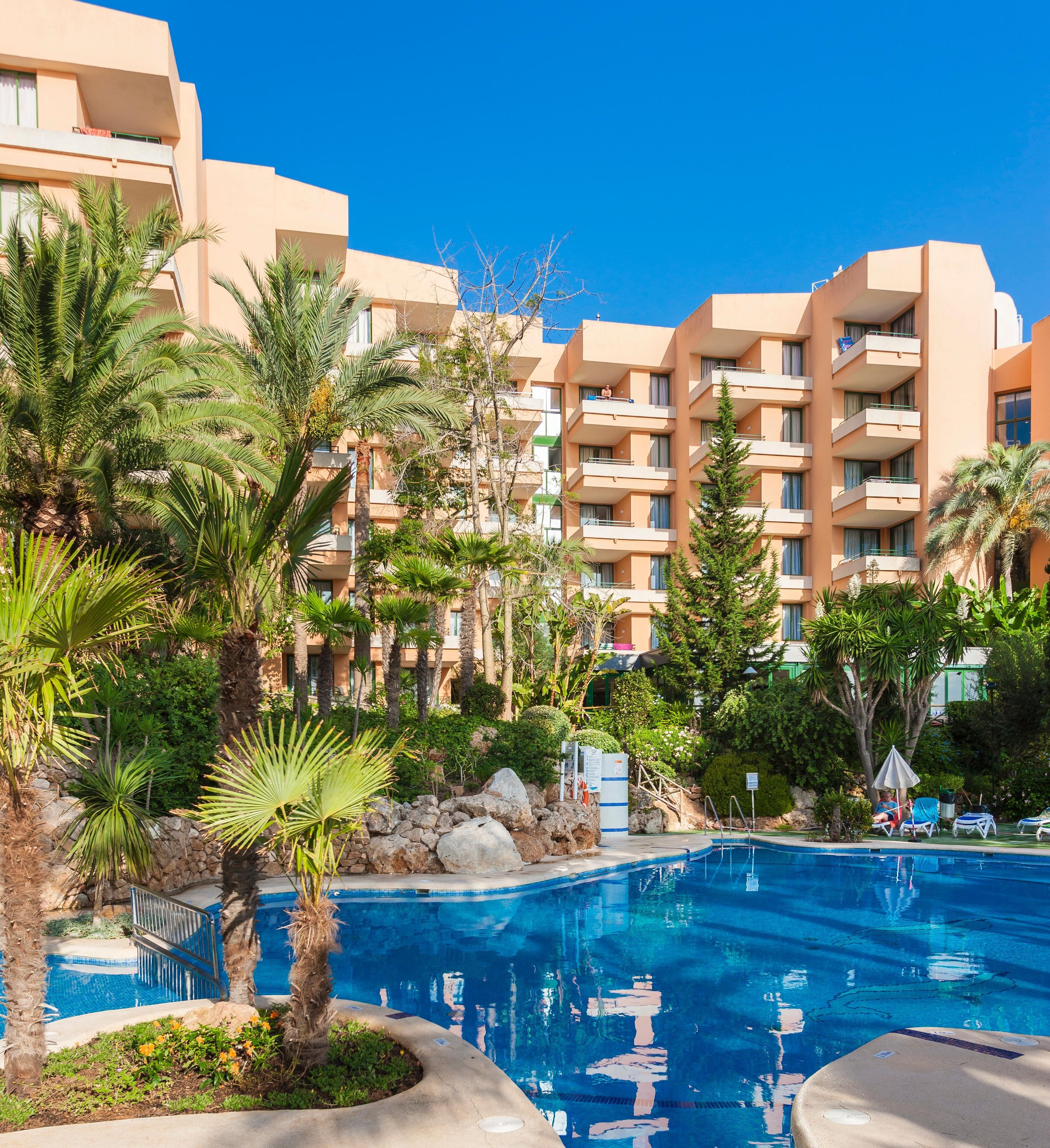 A hotel with a swimming pool surrounded by palm trees and a clear blue sky.