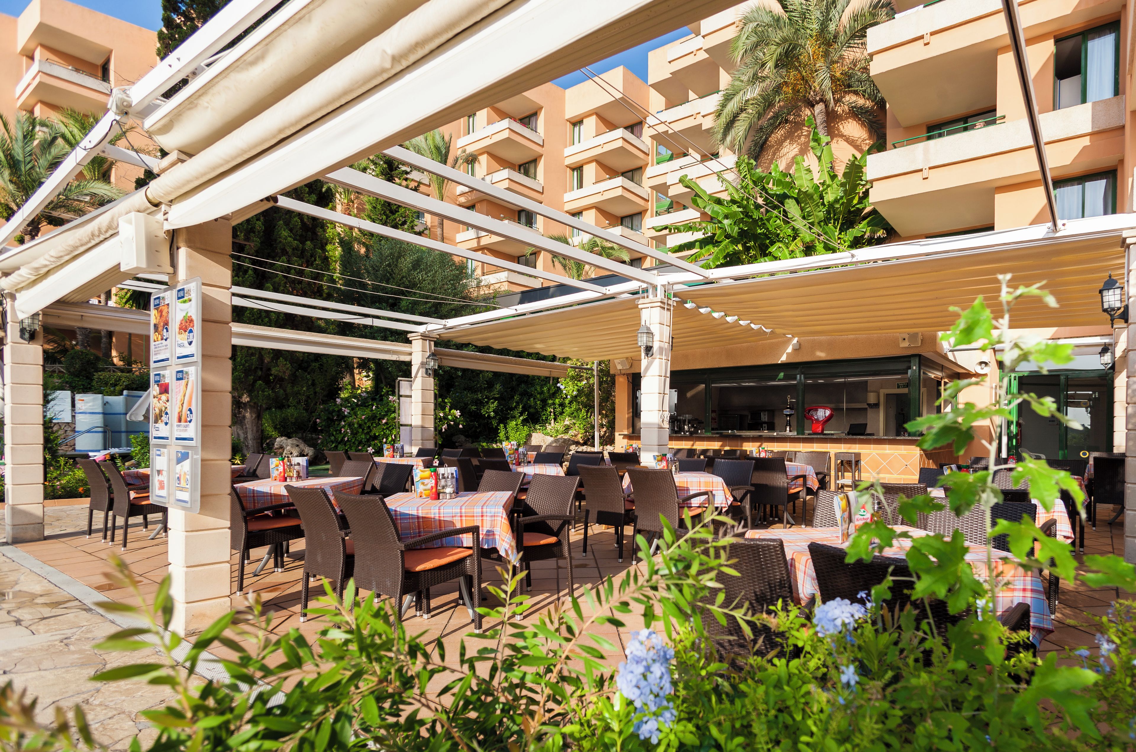 Un patio al aire libre con mesas y sillas, un área de estar cubierta y vistas a un edificio con balcones.