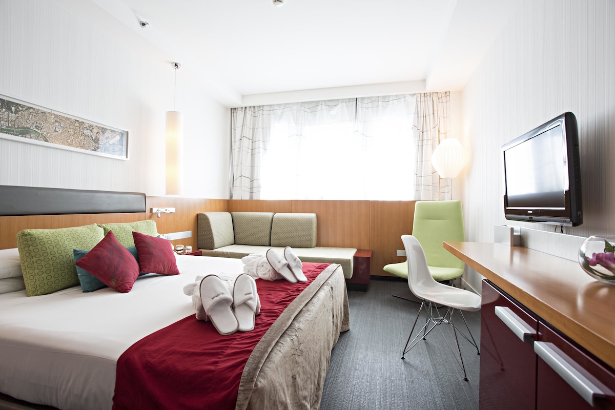 A hotel room with a bed, a desk, a chair, a television, and a window with curtains.