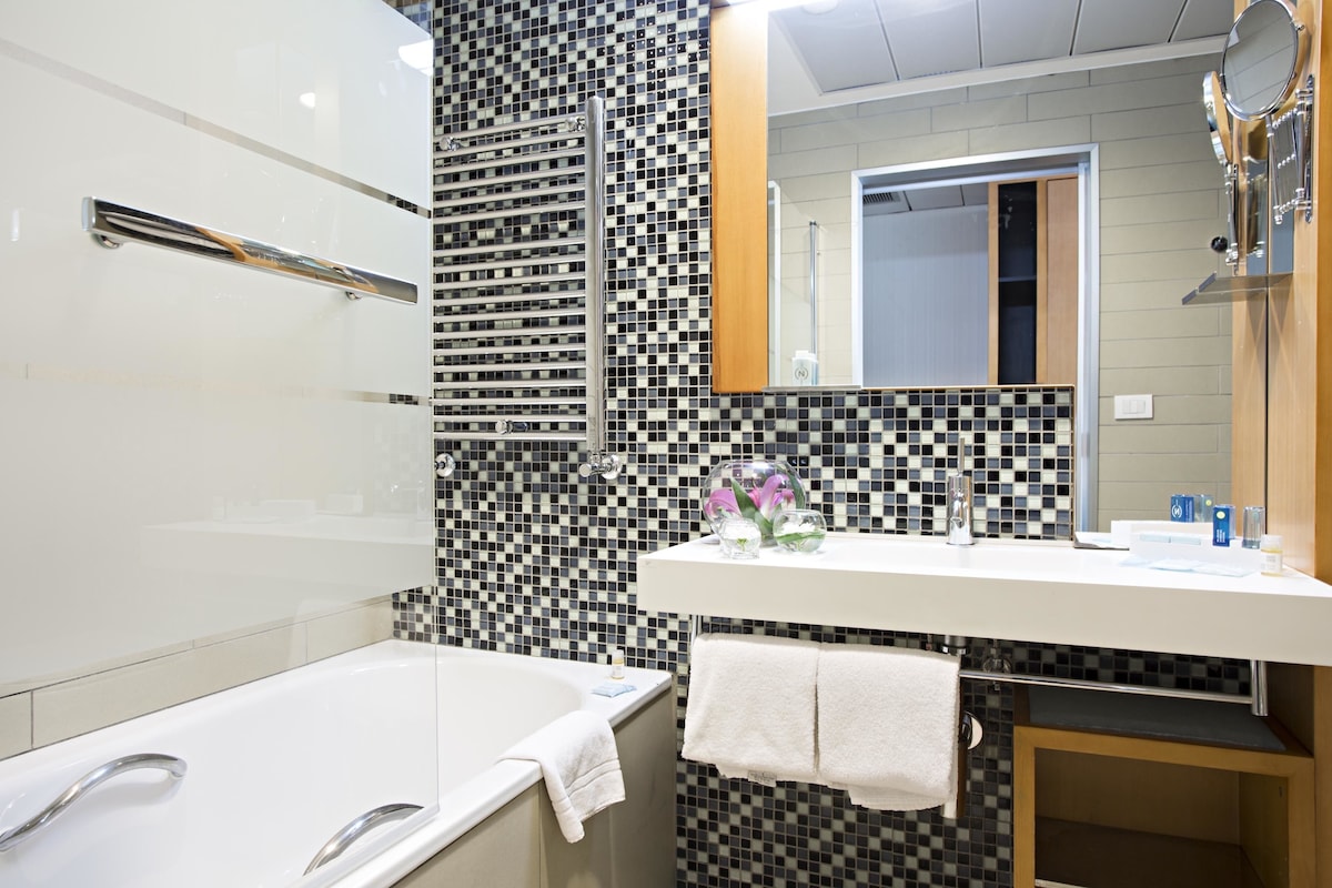 A modern bathroom with a checkered mosaic wall, a white sink with toiletries, a glass-enclosed shower, and a mirror above the sink.