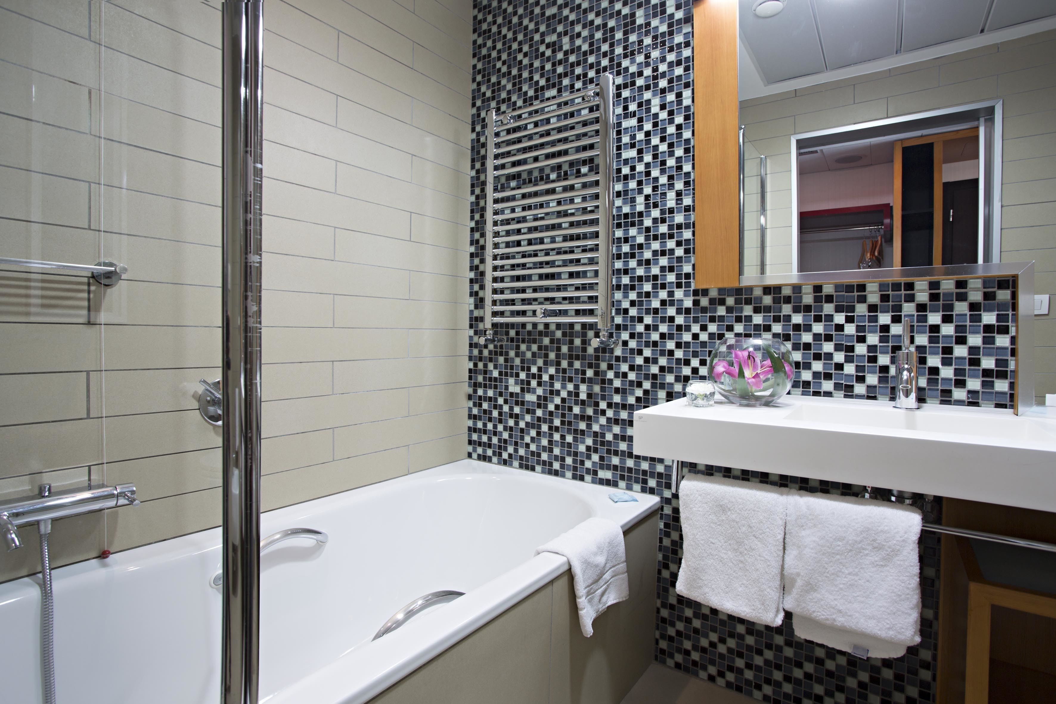 A modern bathroom with a glass-enclosed shower, a white bathtub, and a tiled backsplash.