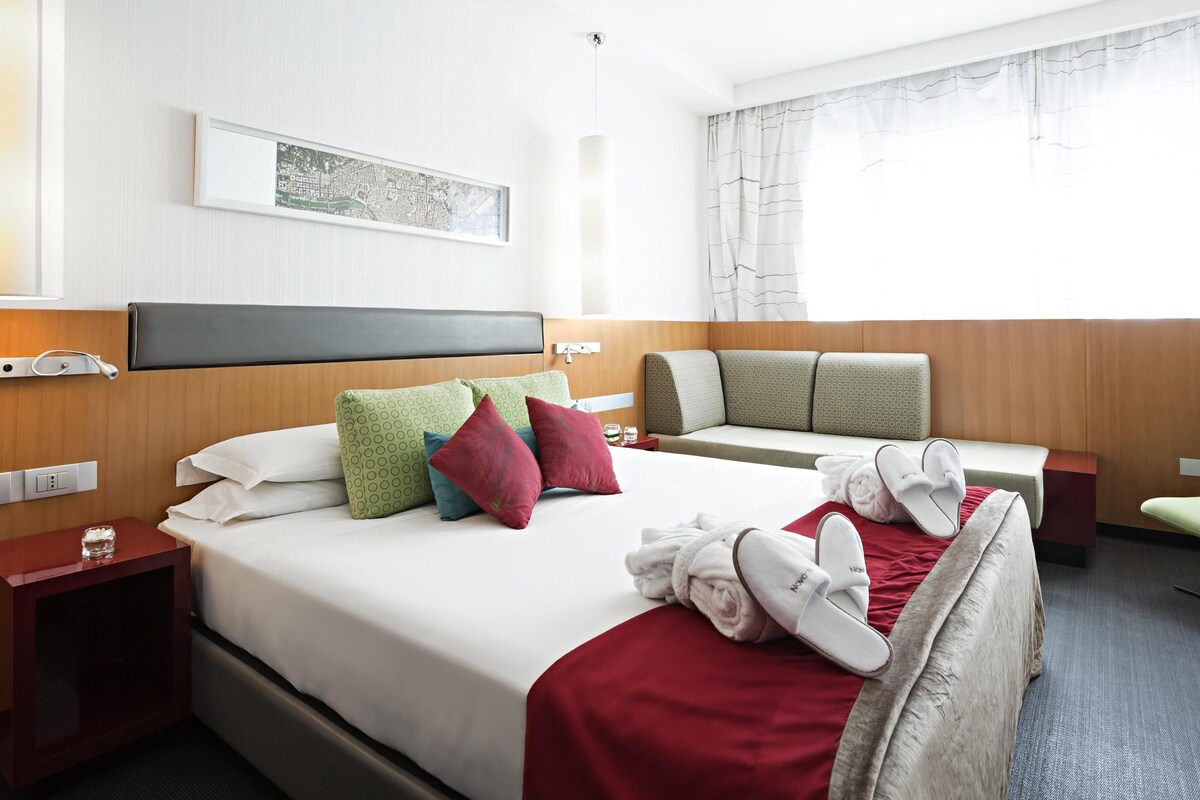 Habitación de hotel con una cama grande, un sofá, una mesita y un televisor de pared.