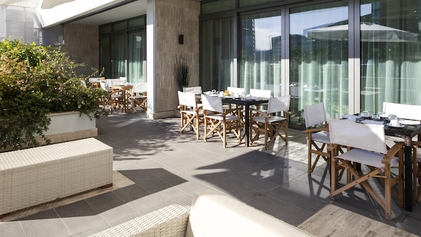 An outdoor patio area with tables and chairs, large windows, and a view of the cityscape. - Novotel Roma Eur (Rome)