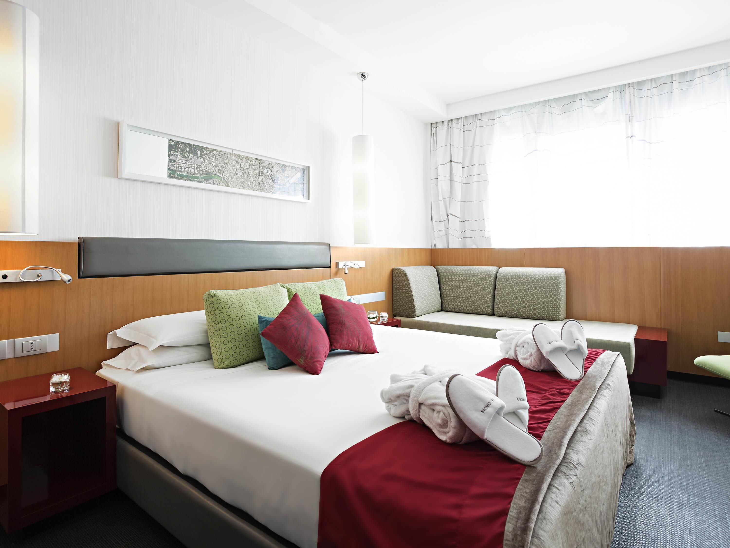 A hotel room with a bed, a sofa, a nightstand, a lamp, and a window with curtains.
