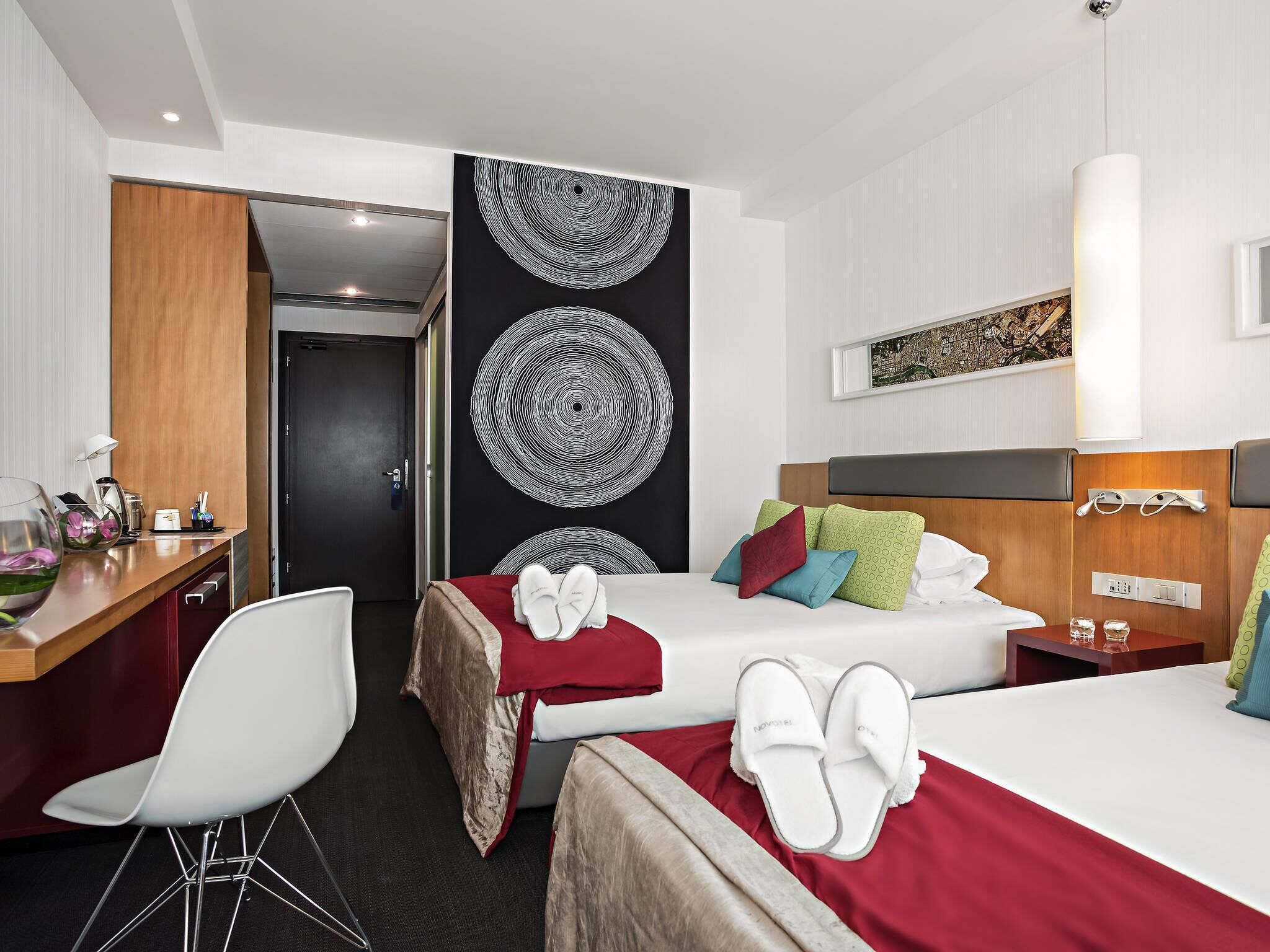 A hotel room with two beds, a desk, a chair, and a large abstract wall art piece.