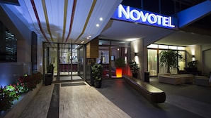 The exterior of a Novotel hotel with a modern design, featuring a prominent illuminated sign, a well-lit entrance, and outdoor seating areas. - Novotel Roma Eur (Rome)