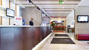 A modern reception area with a reception desk, digital screens, and a seating area. - Novotel Roma Eur (Rome)