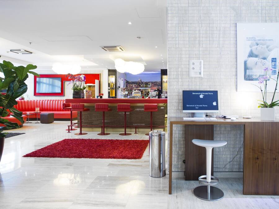 A modern hotel lobby with a red sofa, a bar area, and a reception desk.