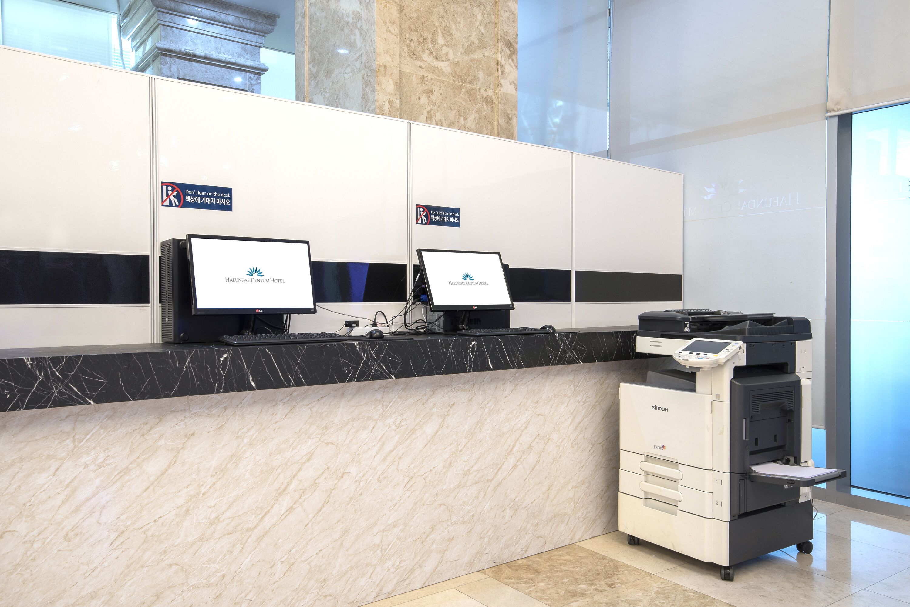 A hotel reception desk with two computer monitors, a printer, and a scale.