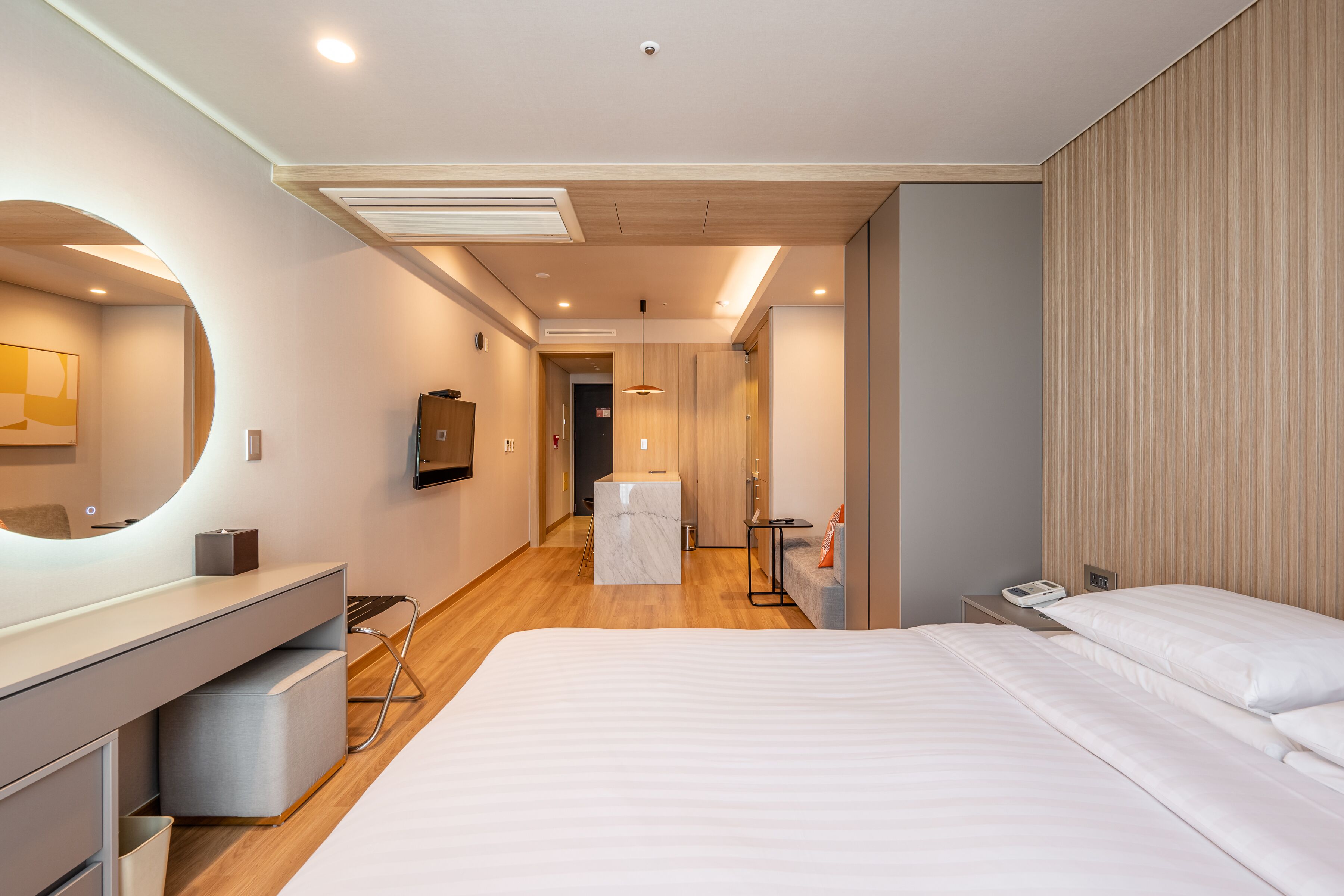 Ein modernes Hotelzimmer mit einem großen Bett, einem Schminktisch mit Spiegel, einem kleinen Tisch und einem Sessel.