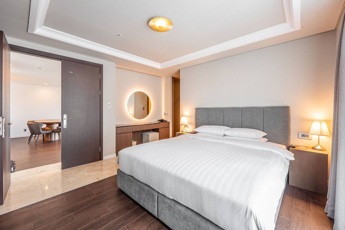 A modern hotel room with a large bed, bedside tables, a mirror, and a desk with a chair.
