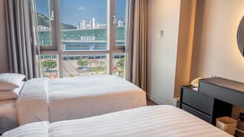 A hotel room with two beds, a desk, and a view of a cityscape including a building labeled 'BEXCO'.