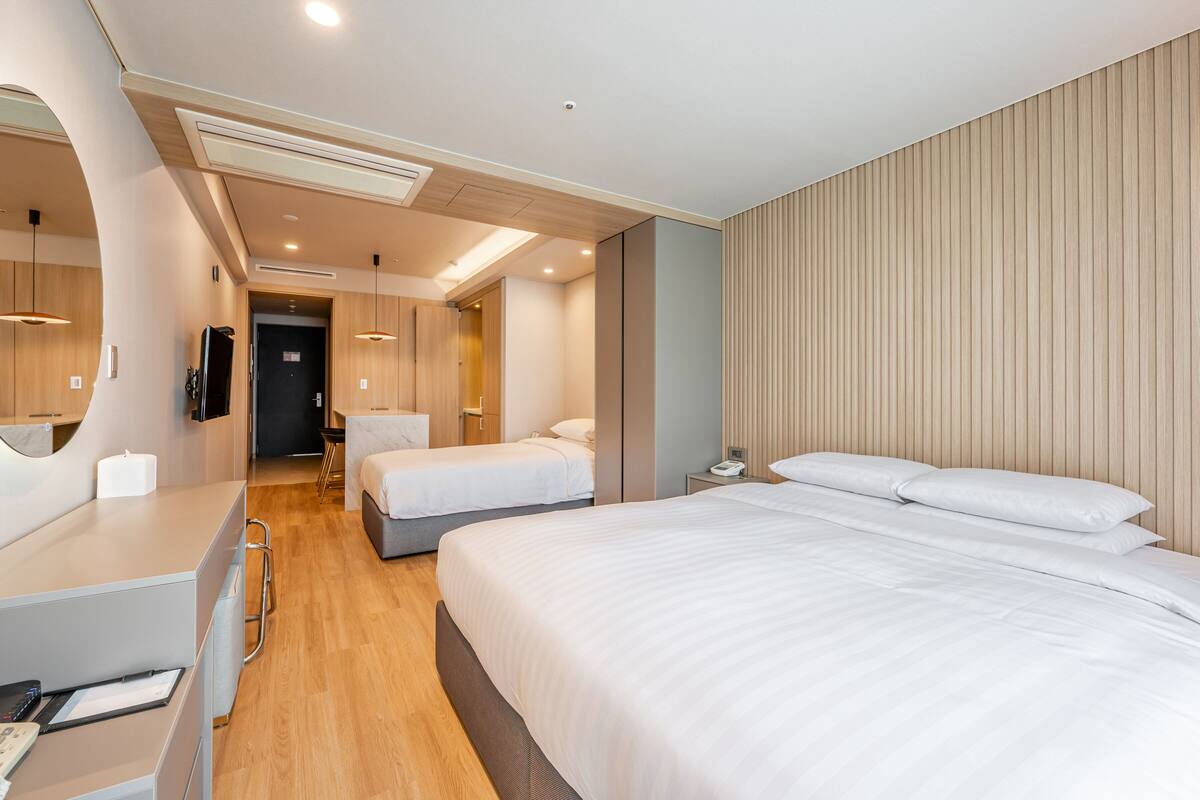 A modern hotel room with a large bed, a desk with a computer, a mirror, and a wooden panel wall.