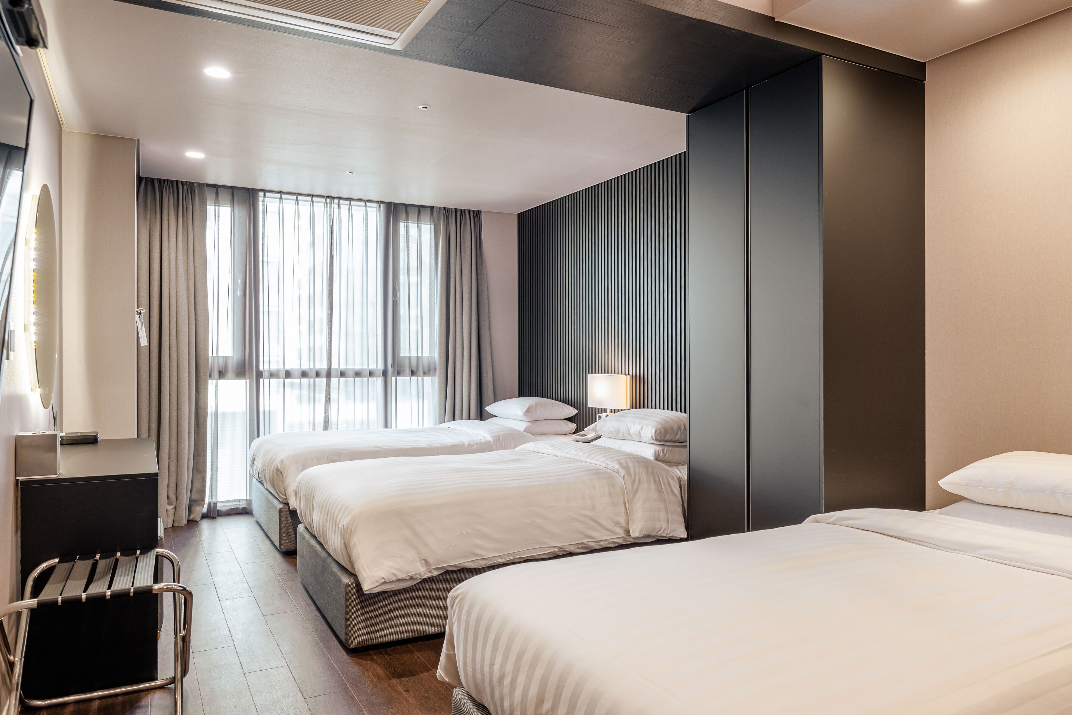 A modern hotel room with two beds, a desk, and a large window with curtains.