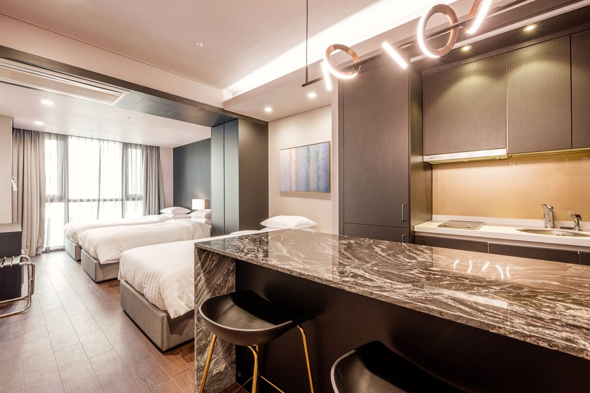 A modern hotel room with a marble countertop, two beds, a large window with curtains, and a separate bathroom area.