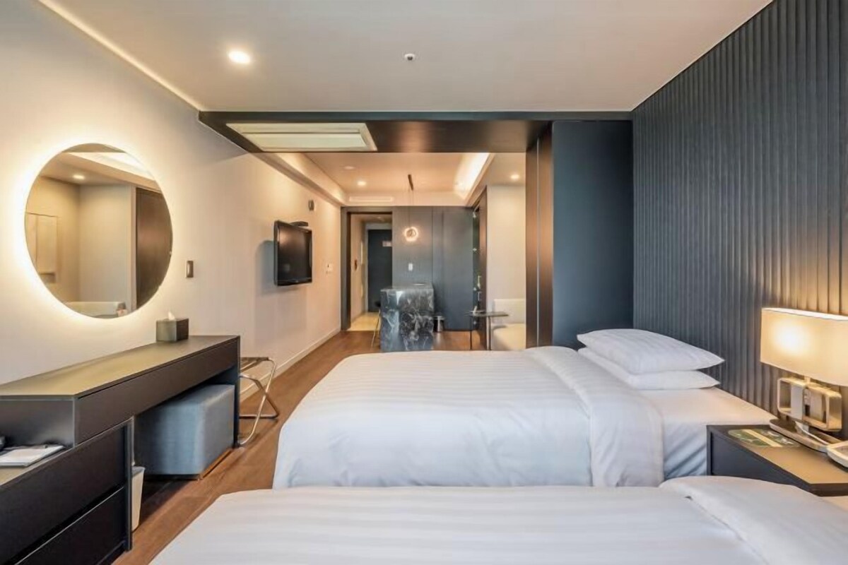 A modern hotel room with a large bed, a bedside table, a mirror, and a bathroom visible through an open door.