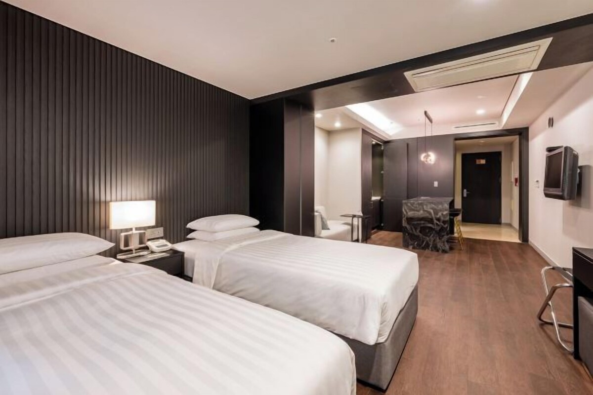 A hotel room with two beds, a desk, a chair, and a TV.