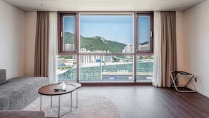 A modern hotel room with a large window, a sofa, a small round table, and a metal chair. - Haeundae Centum Hotel (Busan)