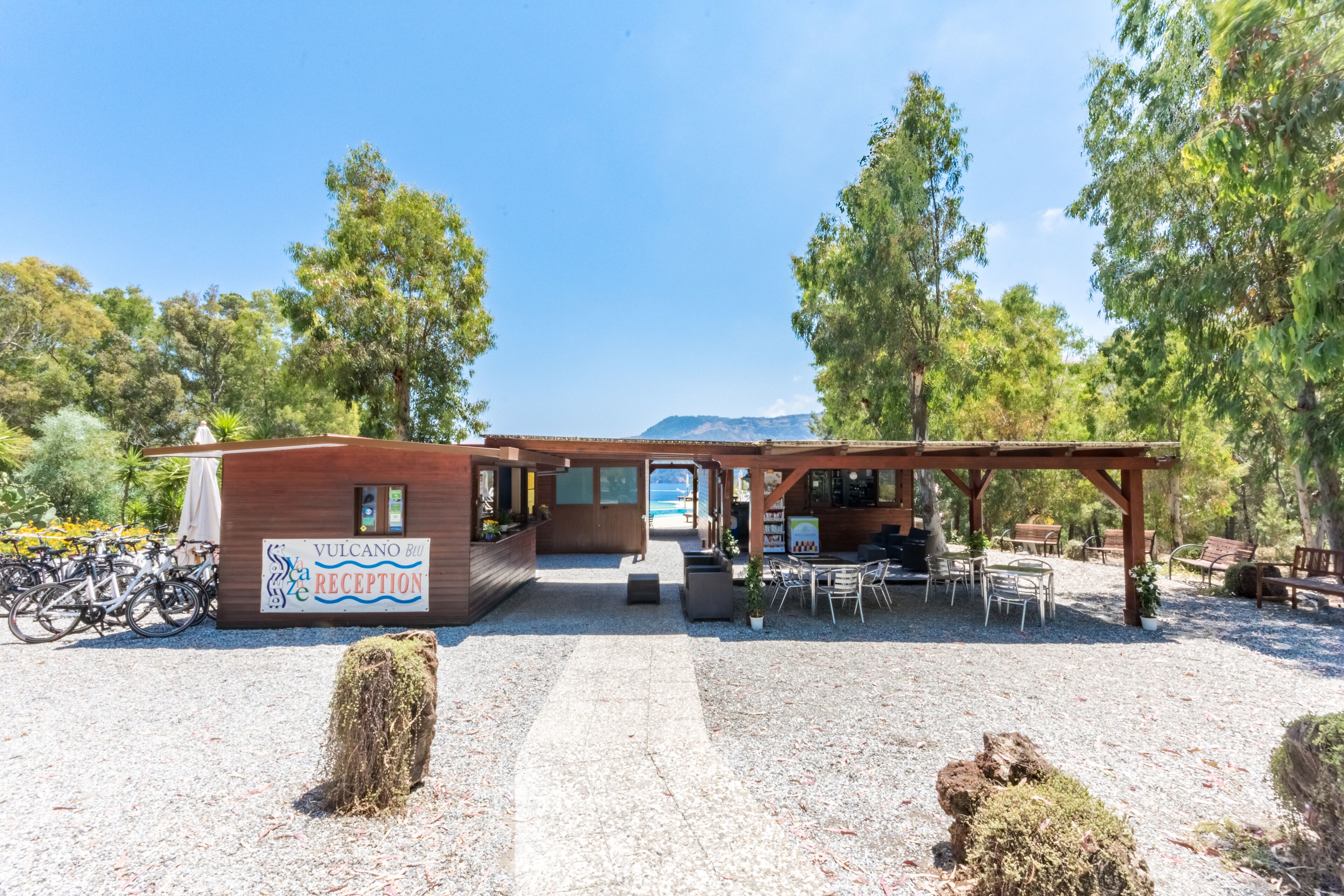 A reception area with a sign reading "Vulcano Bi Reception," outdoor seating, and bicycles parked outside.