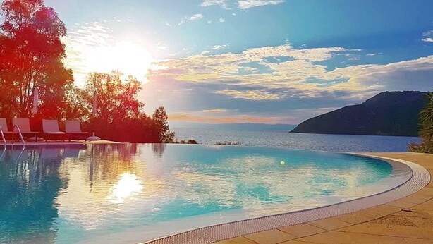 Una piscina de borde curvo, rodeada de sillones de descanso y con vistas al mar y las montañas.