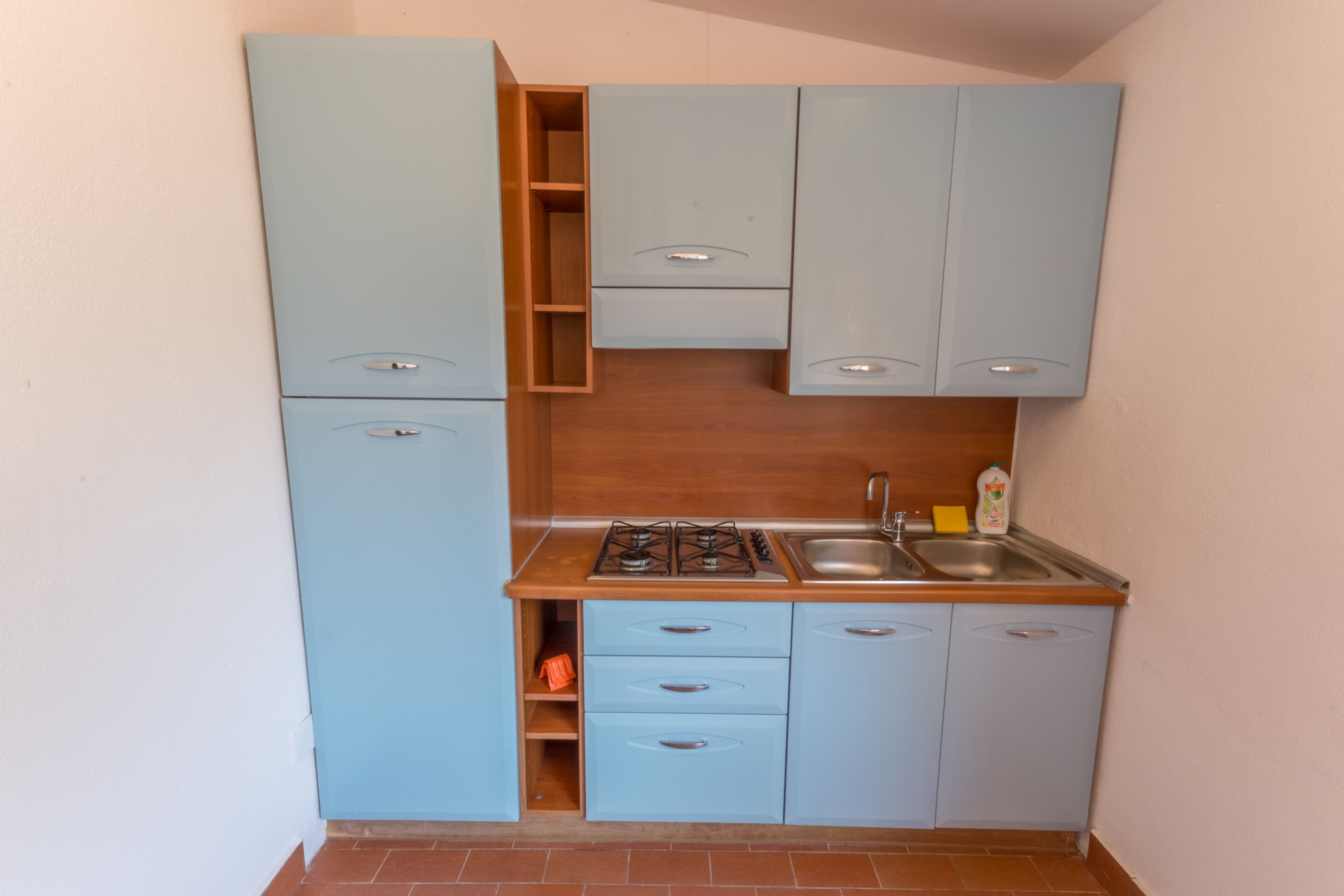 Eine kleine Küche mit hellblauen Schränken, einer Holz Arbeitsplatte, einem Gasherd und einem Spülbecken.