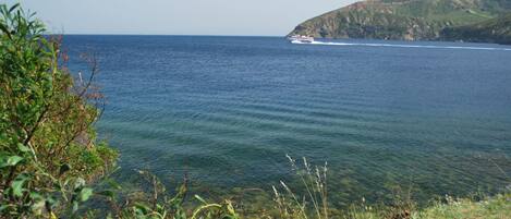 A coastal view with a boat on the water and a hilly landscape in the background.