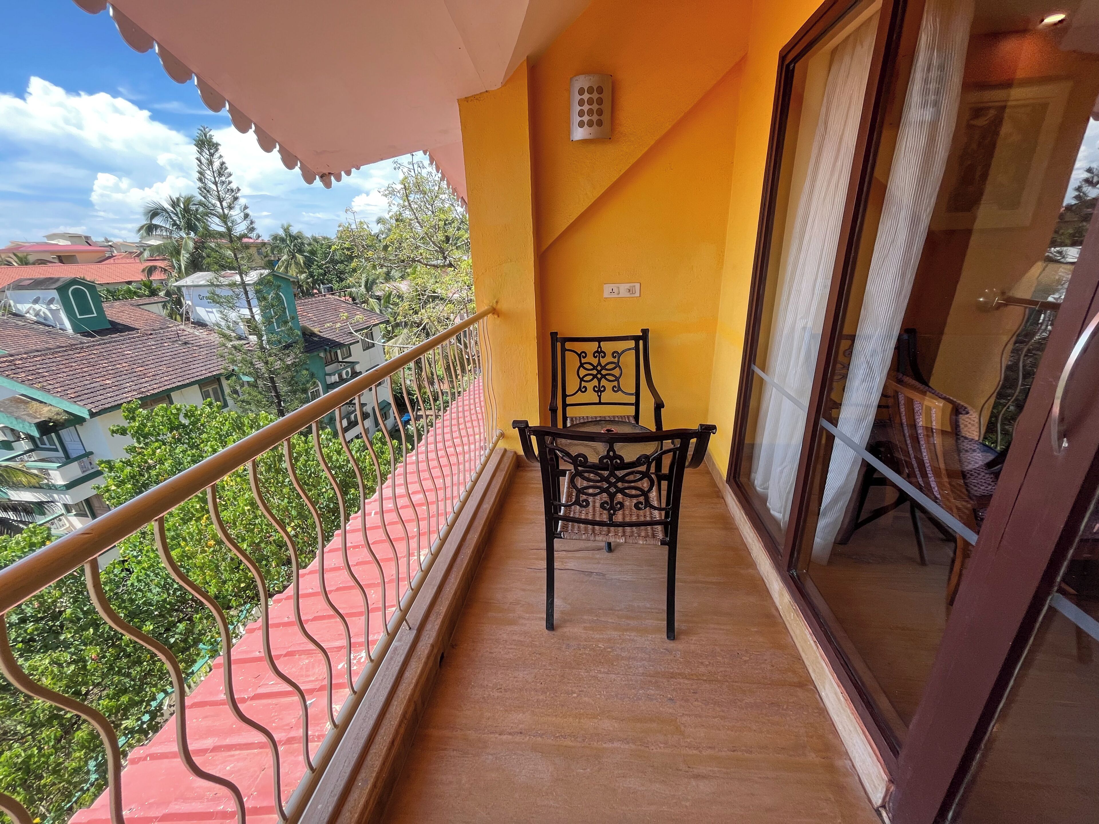 Un balcone con ringhiera rossa, una sedia e vista sugli edifici circostanti.