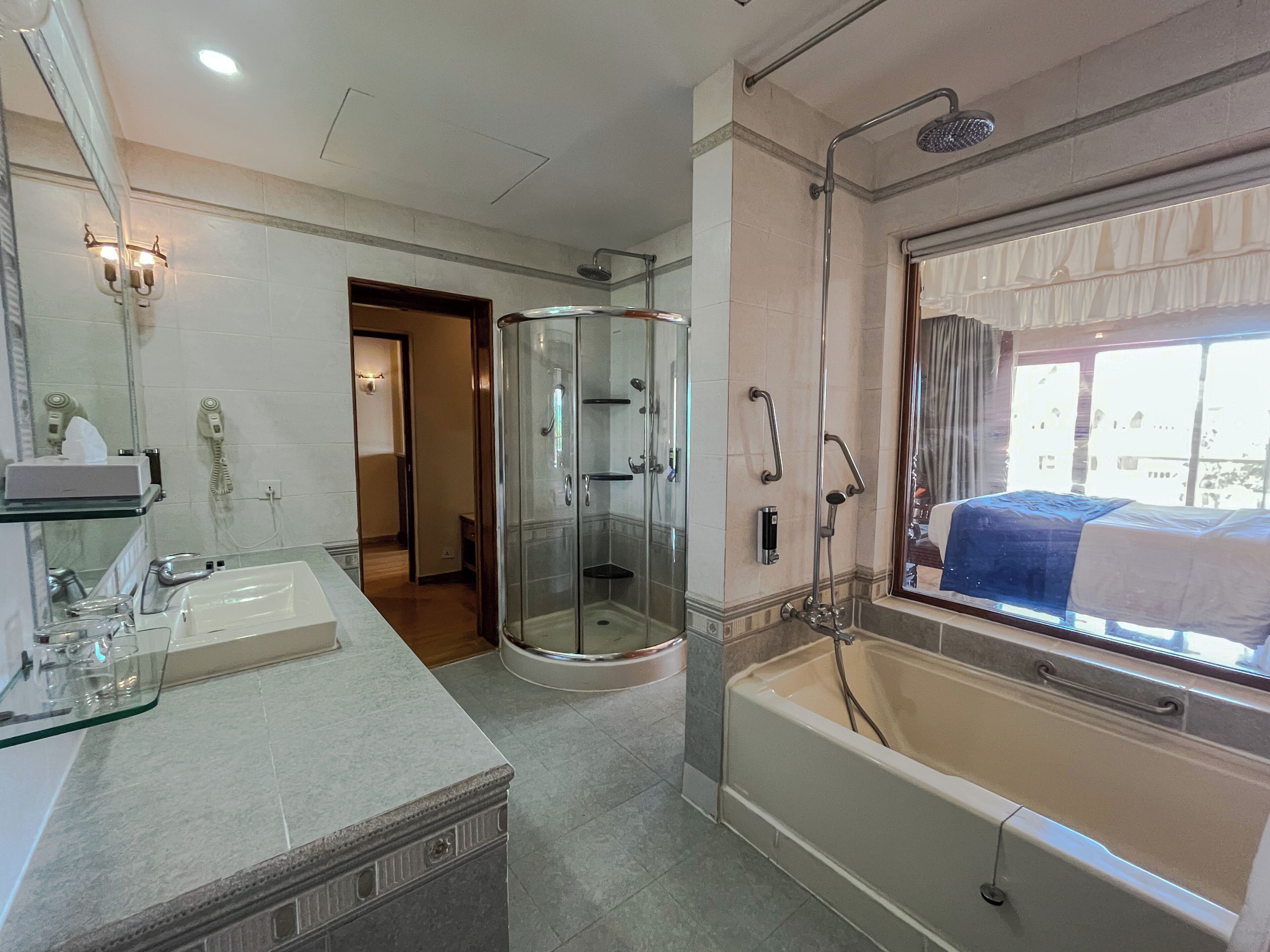 Un baño con ducha de vidrio, bañera, tocador con espejo y ventana con vistas.