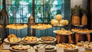 A variety of pastries and fruits displayed on a counter with a view of greenery through a window. - Acron Candolim Regina (Candolim)