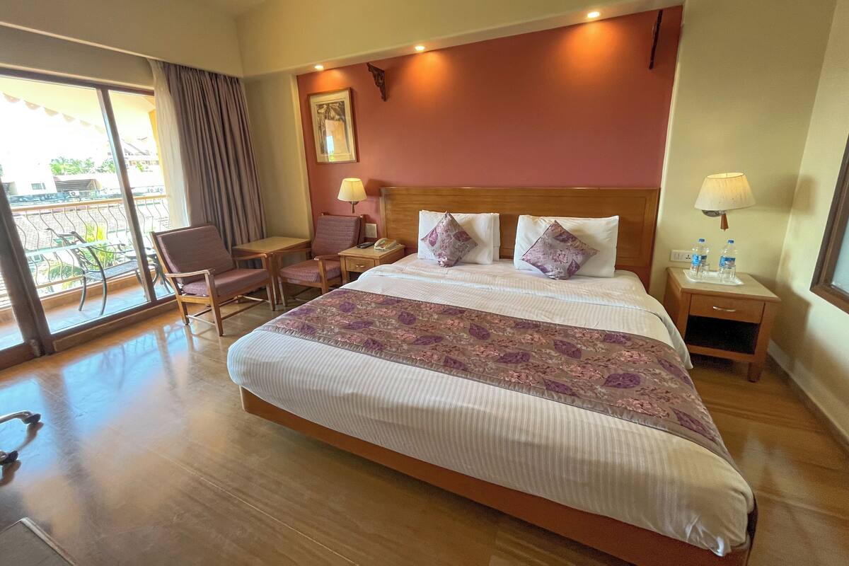 A hotel room with a large bed, a desk, a chair, a nightstand, and a window with a view of the outside.