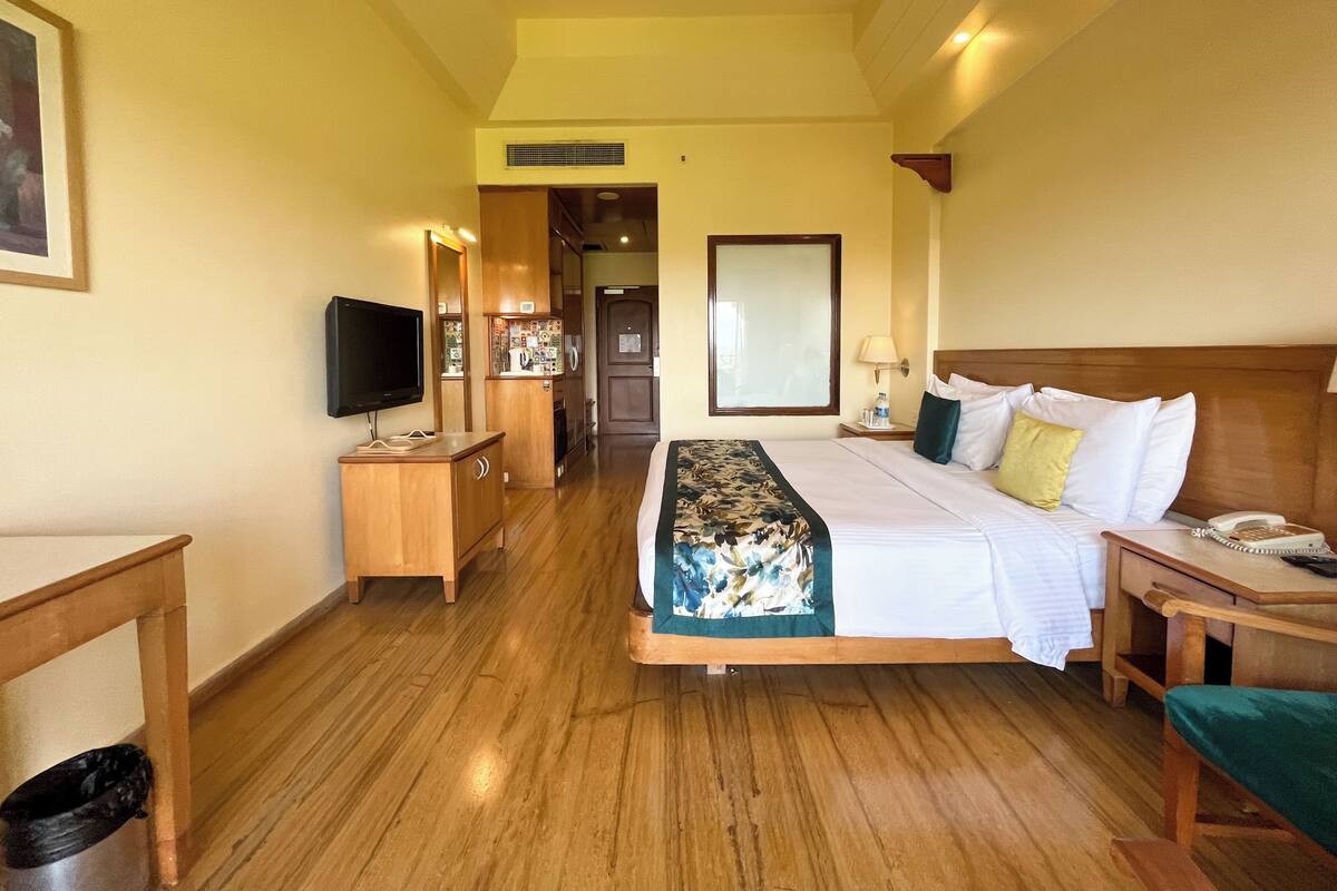 A hotel room with a bed, bedside table, TV, wooden dresser, and a mirror.