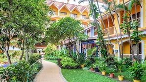 A pathway lined with potted plants leading to a building with balconies and a yellow facade. - Acron Candolim Regina (Candolim)