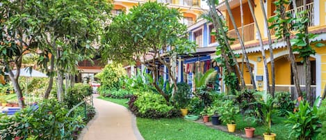 A pathway lined with potted plants leading to a building with balconies and a yellow facade.