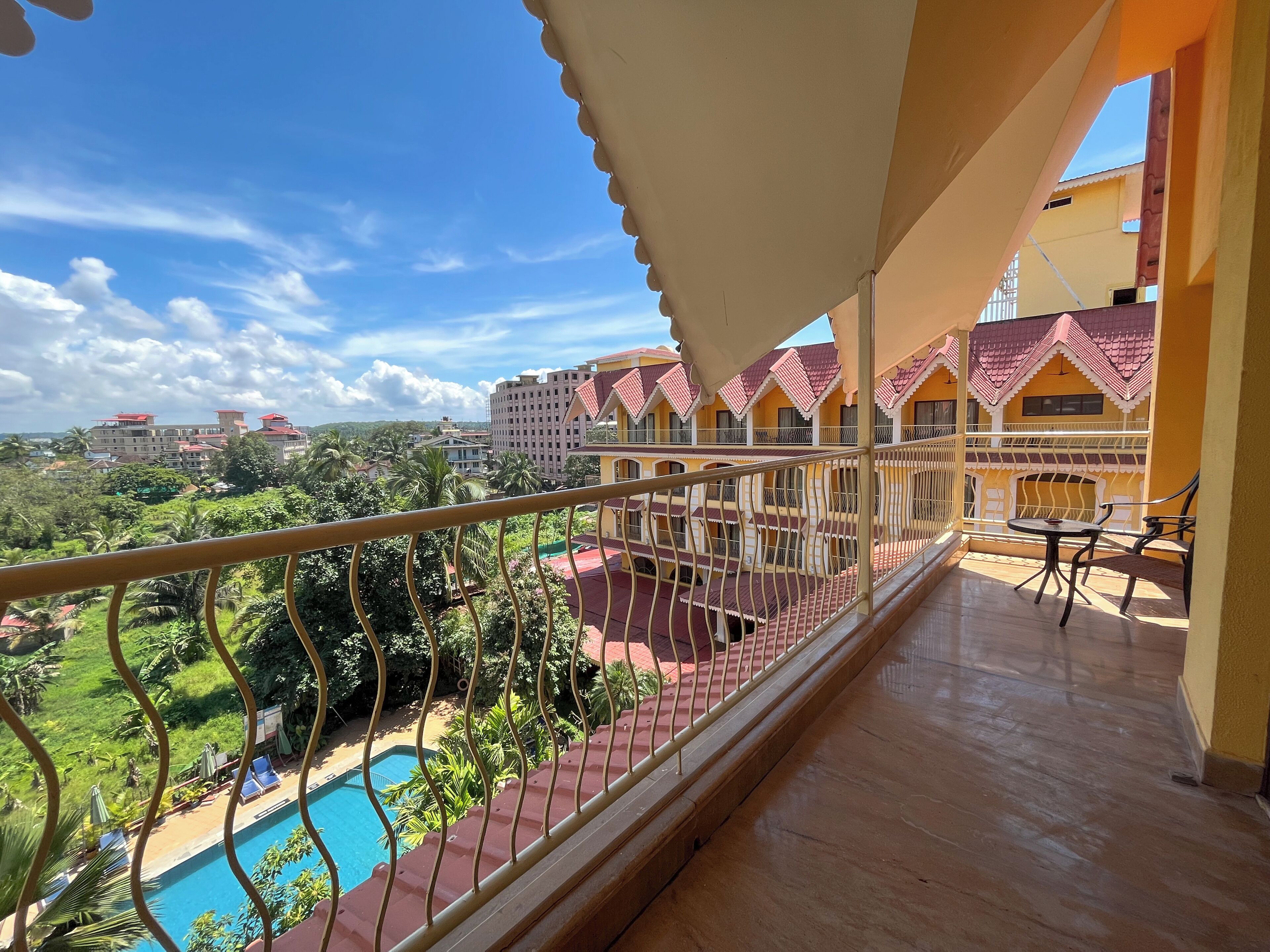 A balcony with a pool, surrounded by greenery and buildings with red roofs.