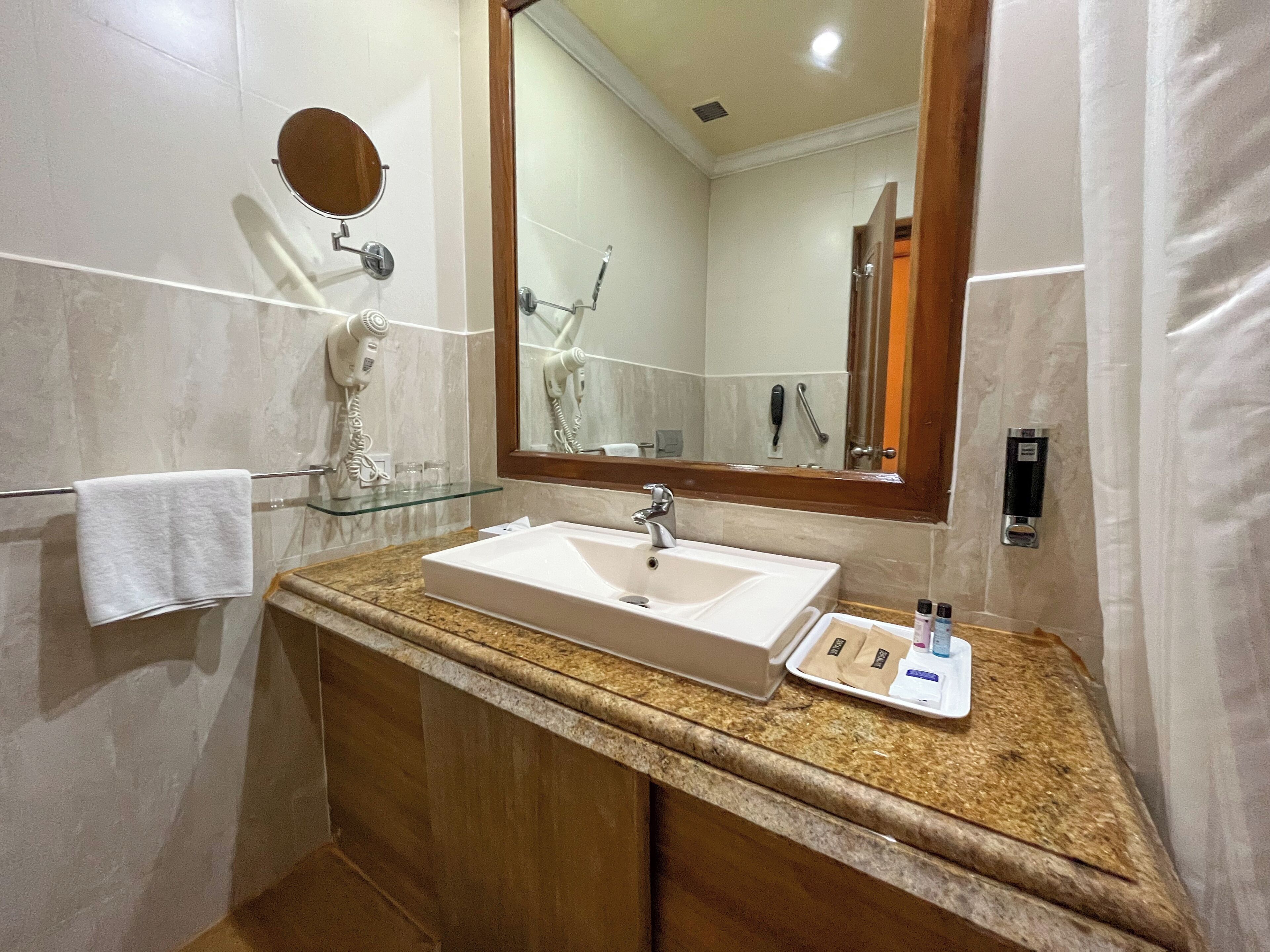 A bathroom with a white sink, a glass shelf, a towel rack, a hairdryer, and a mirror.