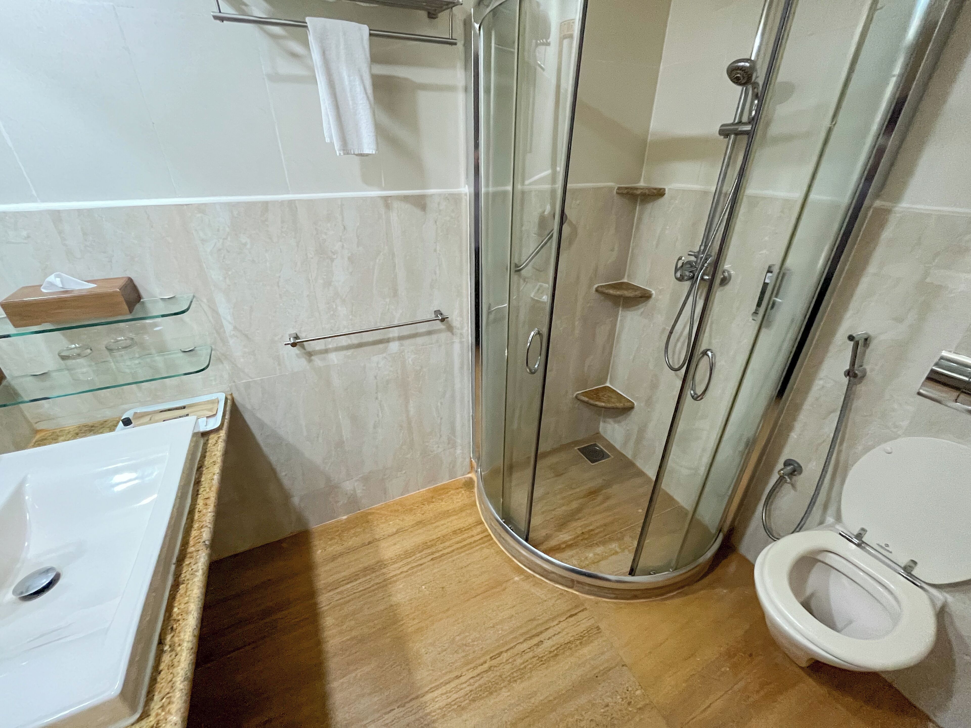 Une salle de bain dotée d’une douche à parois de verre, de toilettes et d’un lavabo avec une étagère en verre.