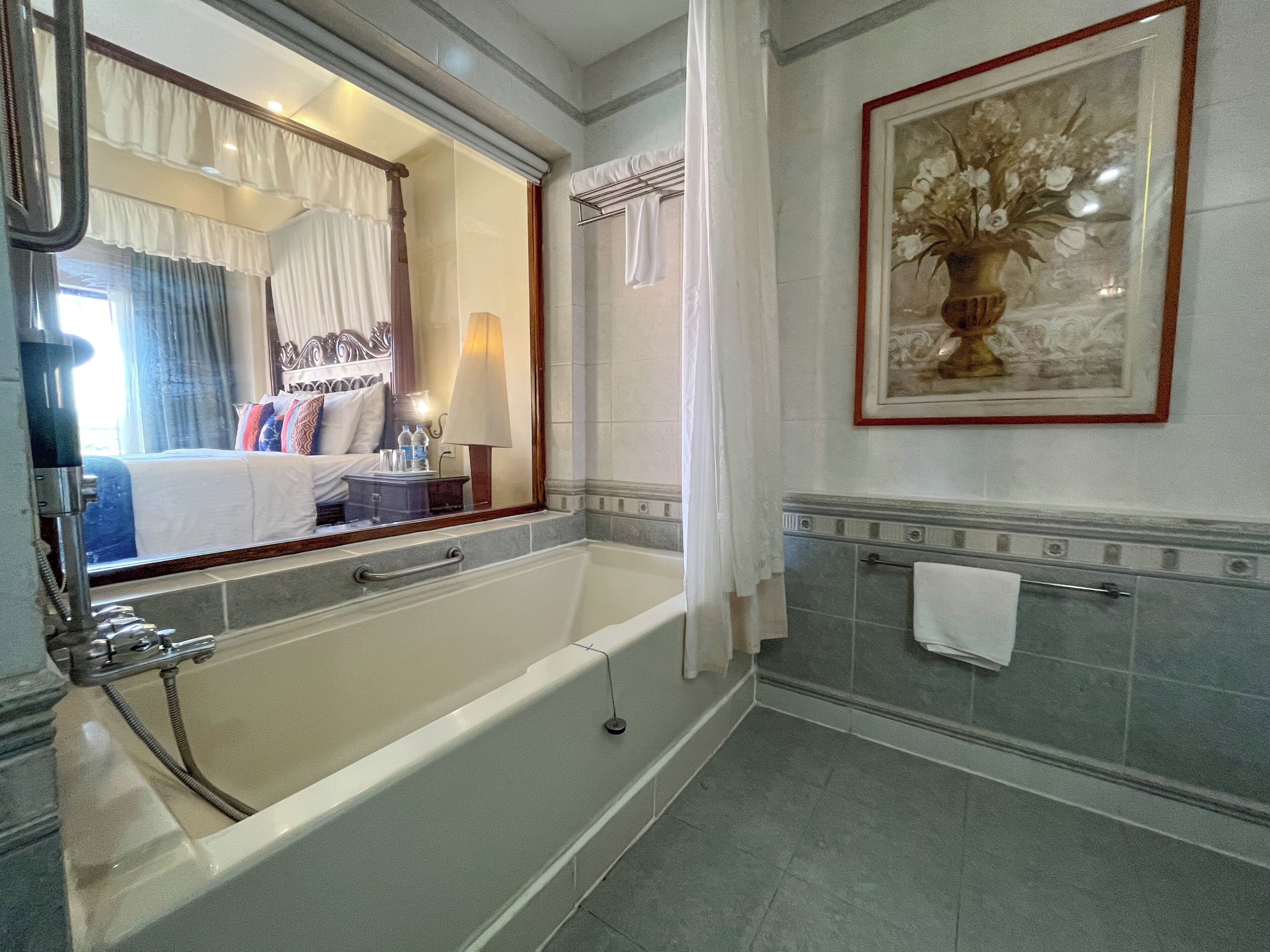 A bathroom with a bathtub, a large mirror, a framed floral artwork, and a towel rack.