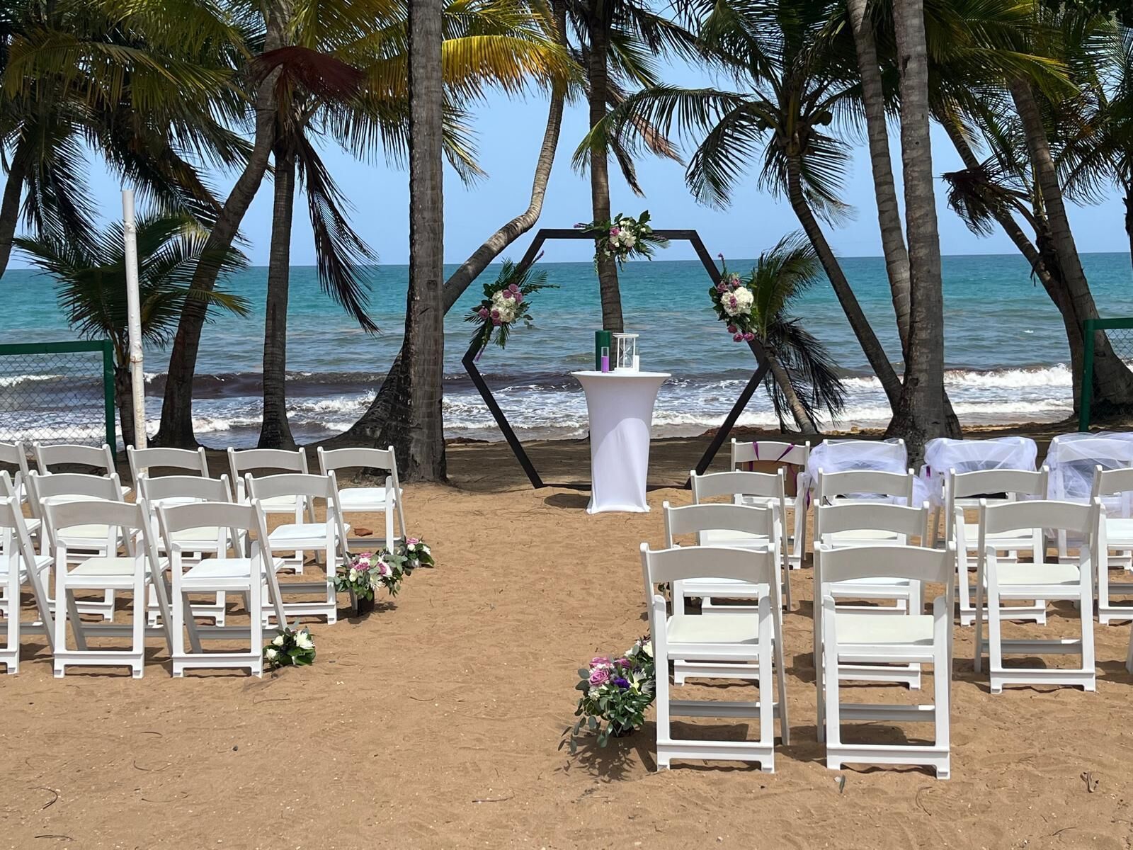Montaje para una boda en la playa, con sillas y una mesa blancos, decorados con flores.