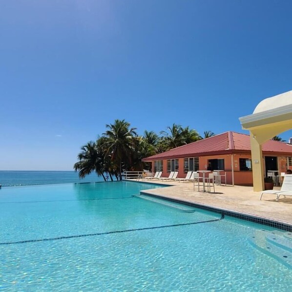 A clear blue pool with lounge chairs and a building with a red roof. - Parador MaunaCaribe (Maunabo)