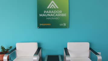 A sign for 'Parador Maunaco' with two white chairs and a small table against a turquoise wall.