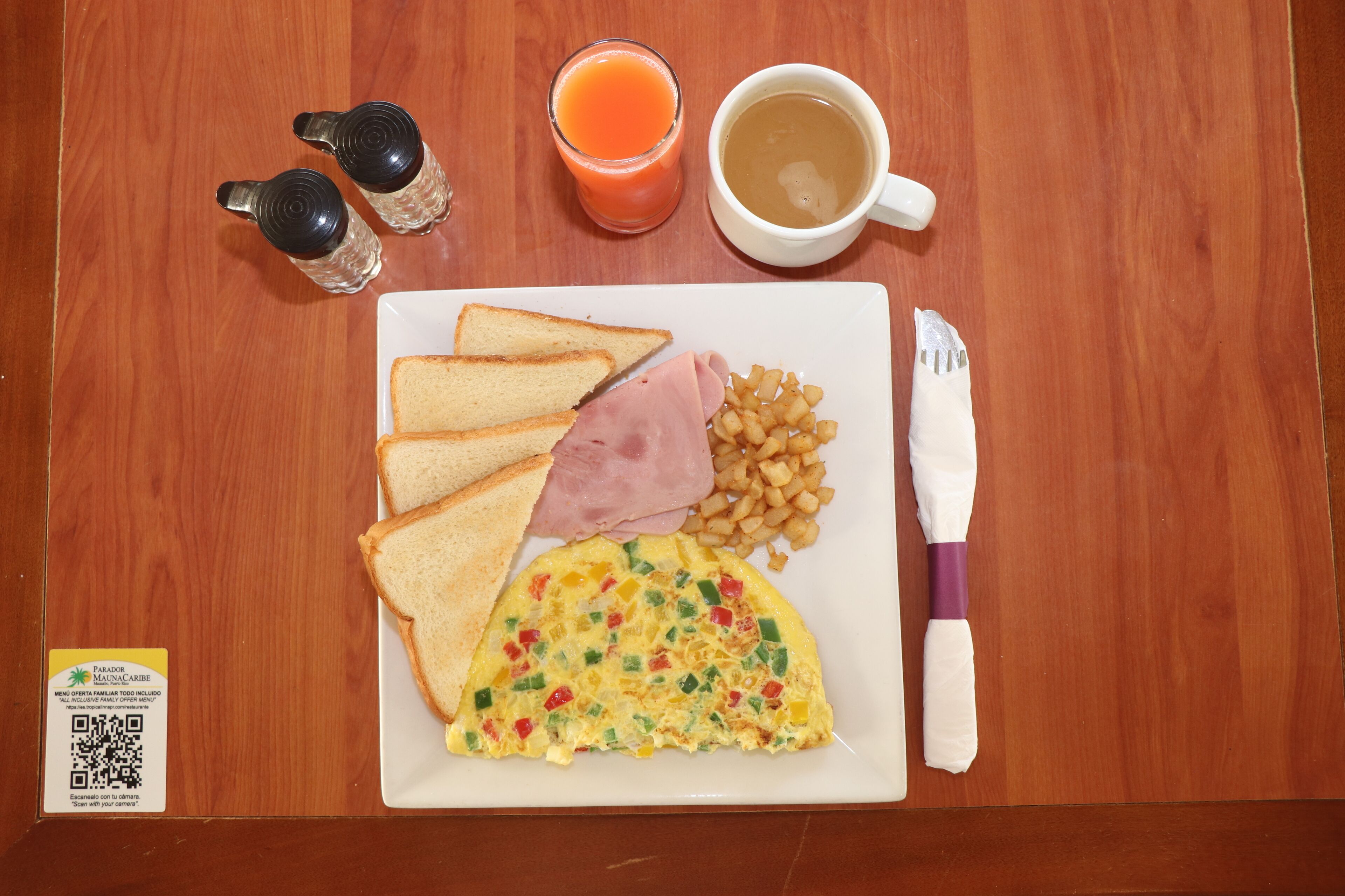 Ein Frühstücksteller mit Toast, Schinken, Bohnen und einem Omelett auf einer Holztischplatte.