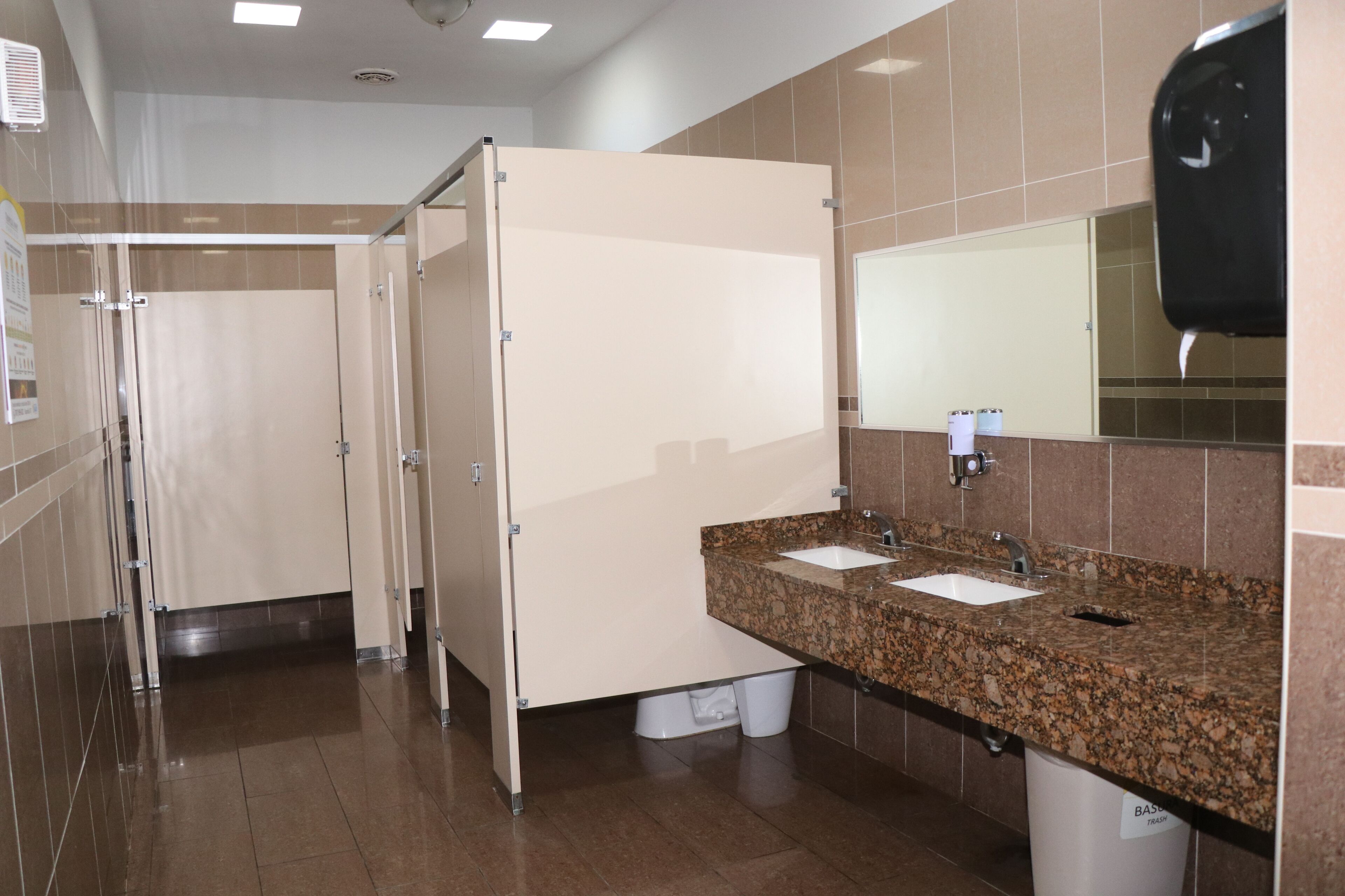 Baño con dos lavamanos, un espejo y un cubo de basura.