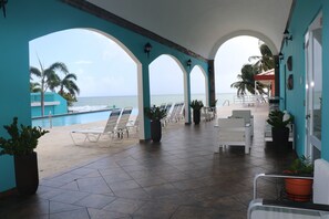 A covered outdoor area with a view of the ocean, featuring lounge chairs, potted plants, and a tiled floor. - Parador MaunaCaribe (Maunabo)