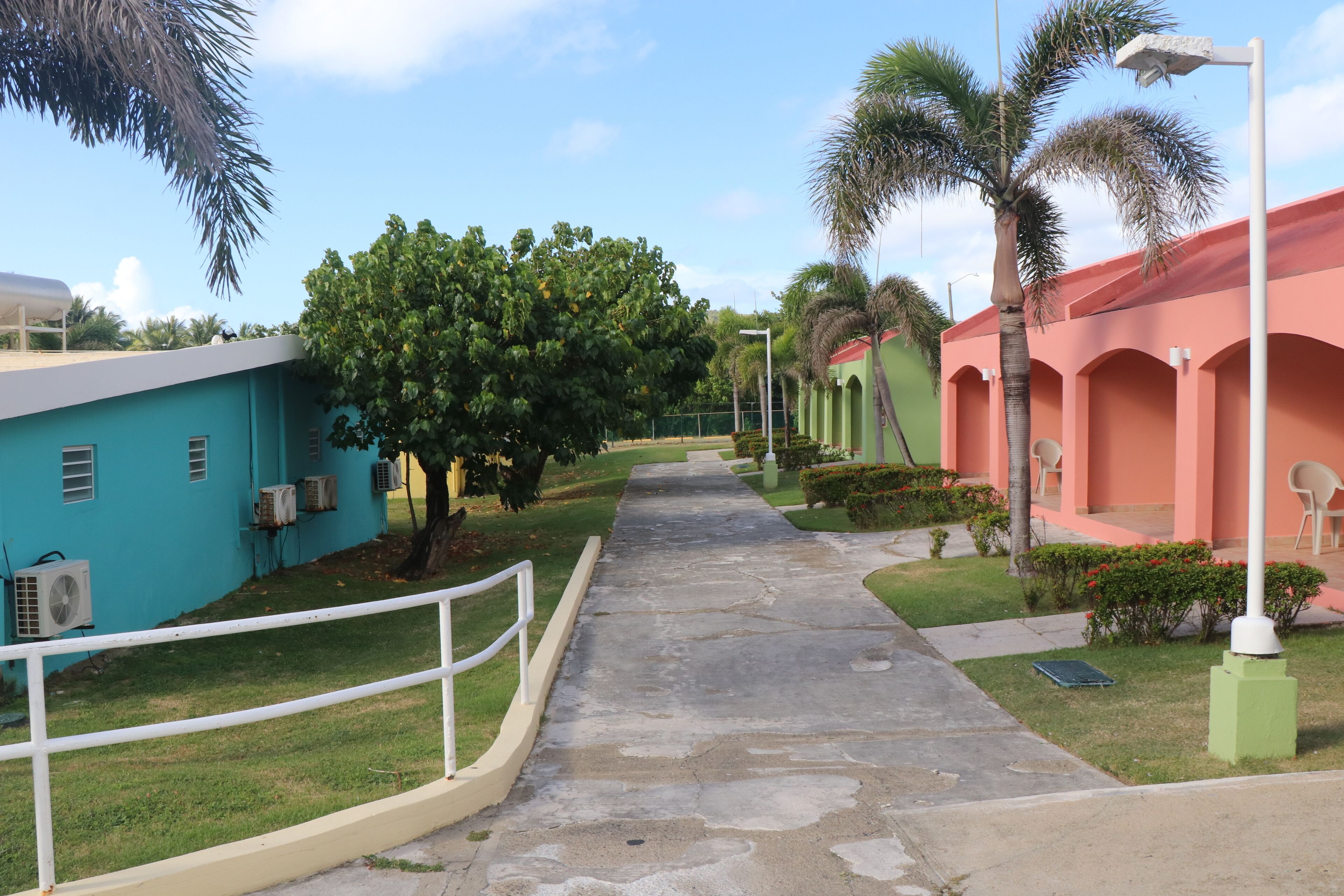 A pathway leading to a building with a blue exterior and air conditioning units.