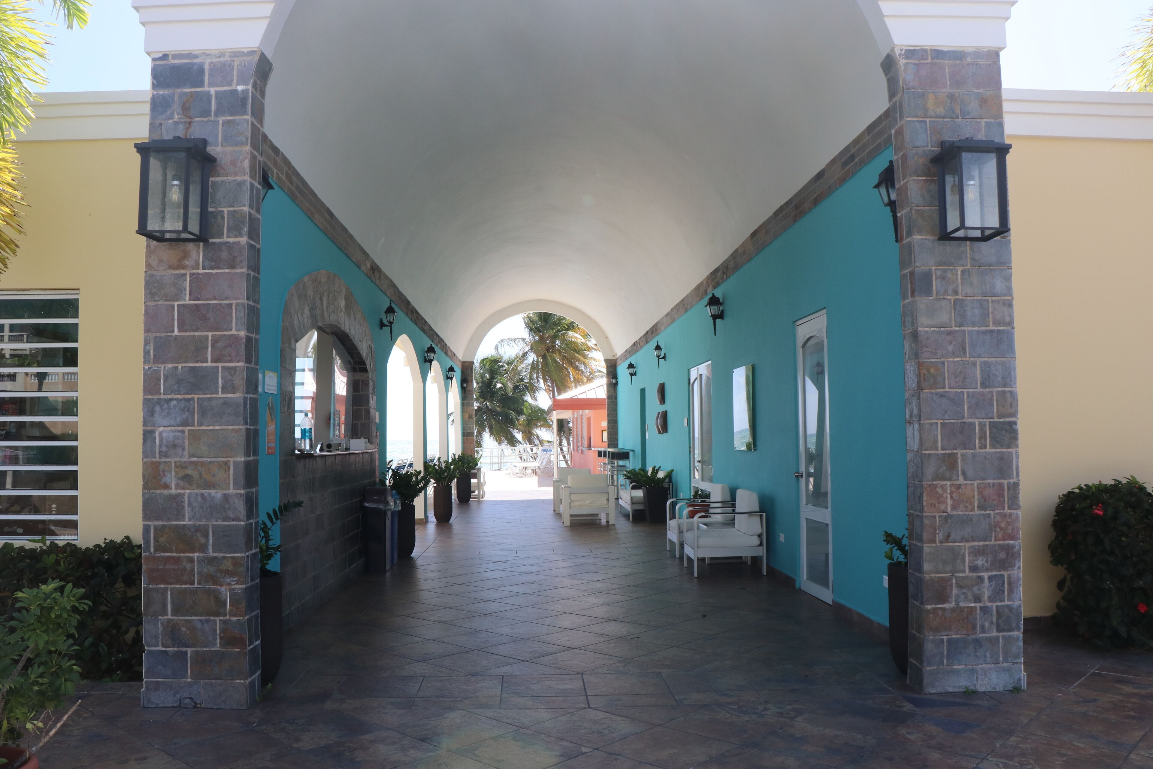 A covered corridor with stone pillars, tiled flooring, and potted plants.