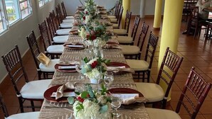 A long dining table with red and white tableware, white chairs, and a floral centerpiece. - Parador MaunaCaribe (Maunabo)