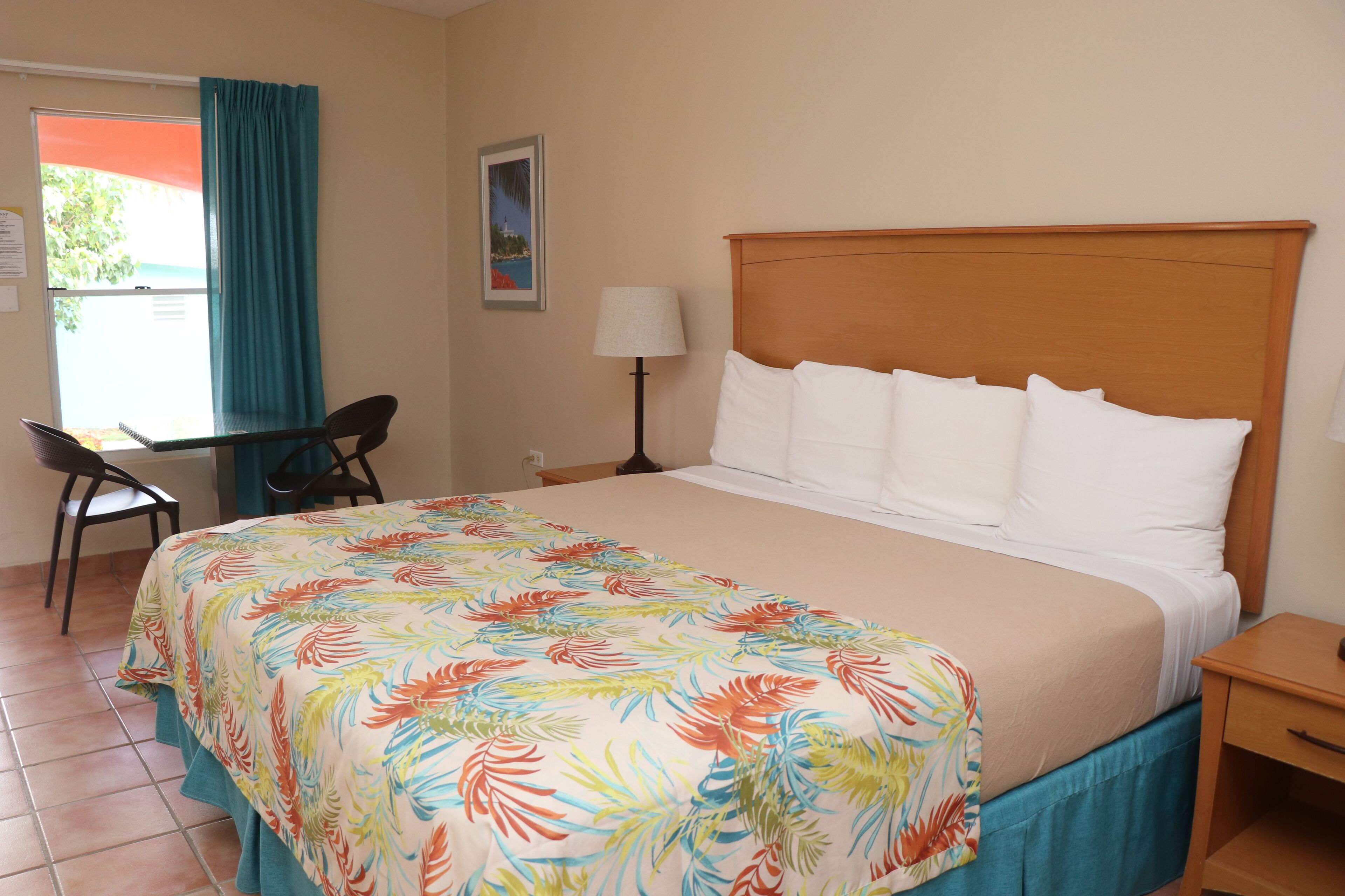 A hotel room with a bed, a desk, a chair, a lamp, and a window with curtains.