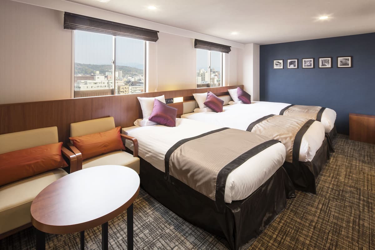 Ein Hotelzimmer mit zwei Betten, einem Sofa, einem kleinen Tisch und Blick auf die Stadt.