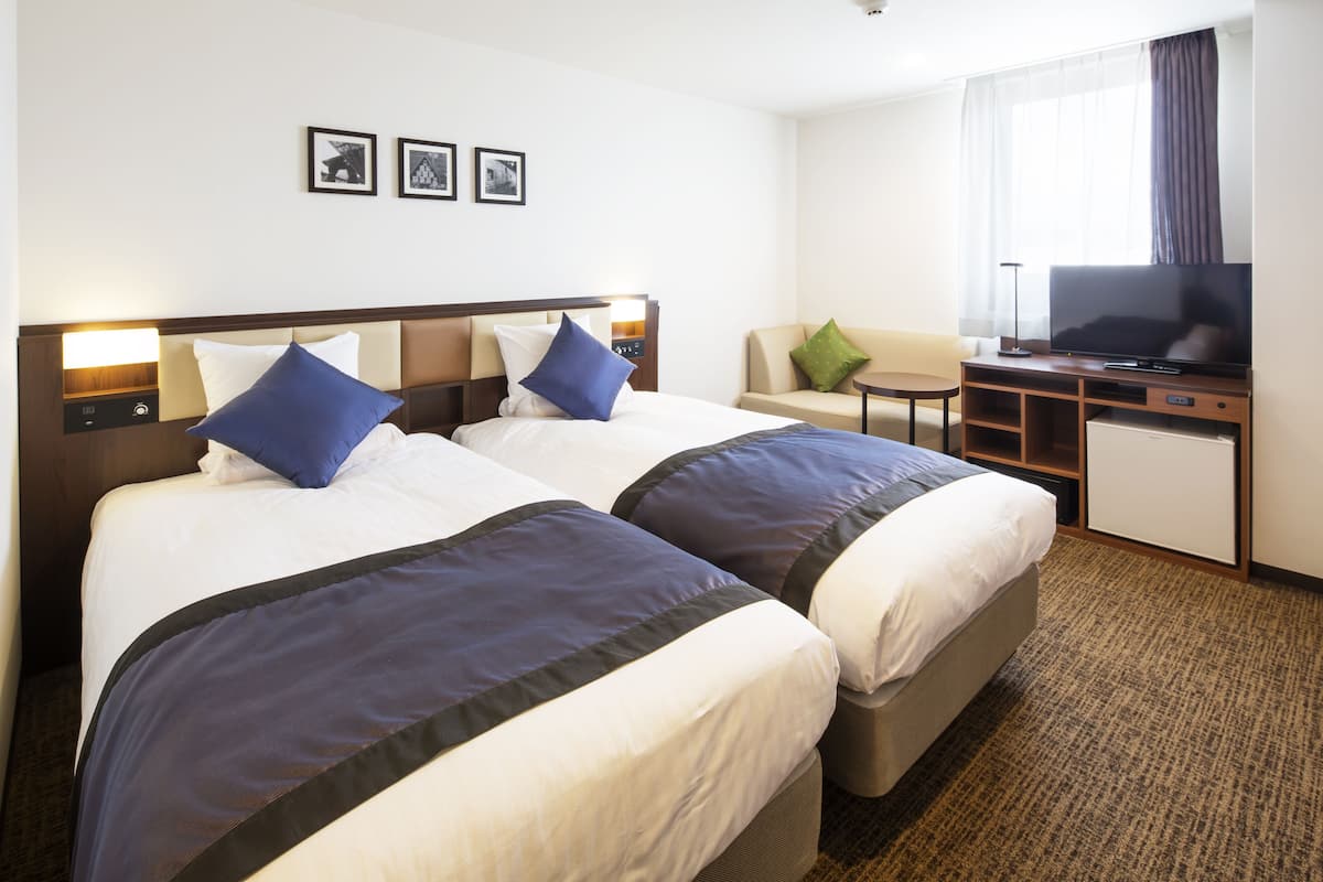 Ein Hotelzimmer mit zwei Betten, einem Schreibtisch mit Fernseher und einer kleinen Sitzecke.