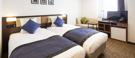 A hotel room with two beds, a desk with a TV, and a small seating area.